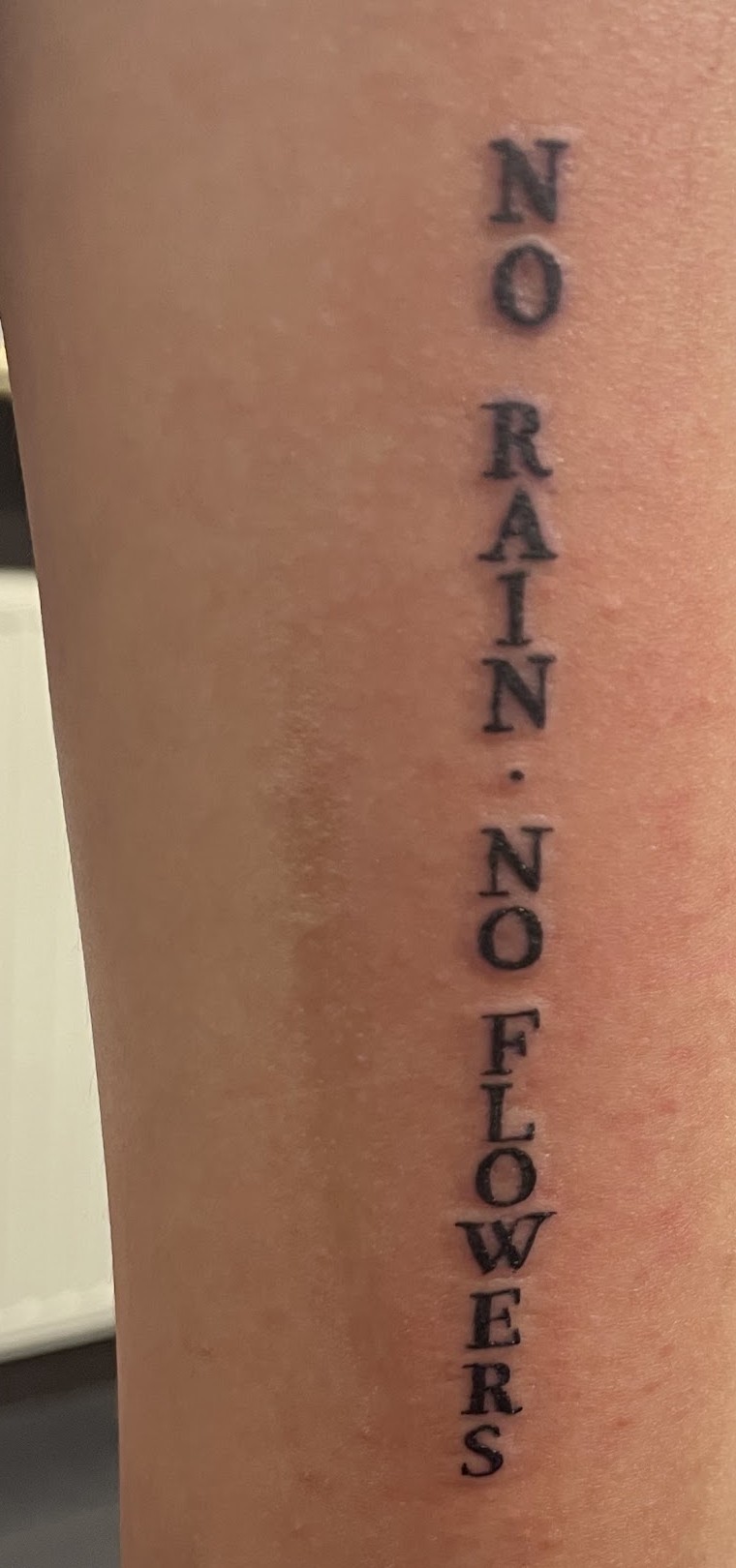 Lettering NO RAIN NO FLOWERS verticaal op een bovenarm